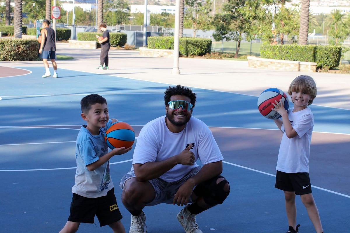 Coach Mike with two young athletes holding basketballs, all smiling