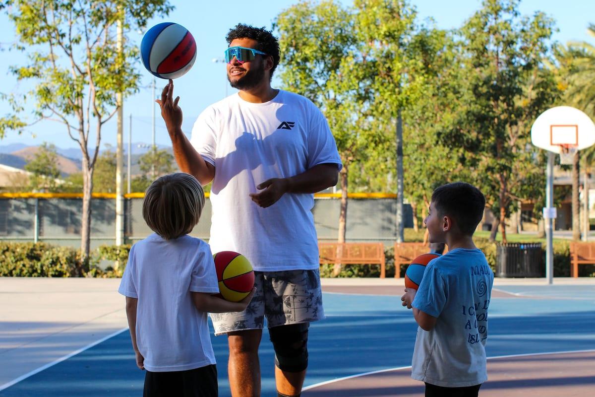 Coach Mike spinning a basketball on his finger as two young athletes watch