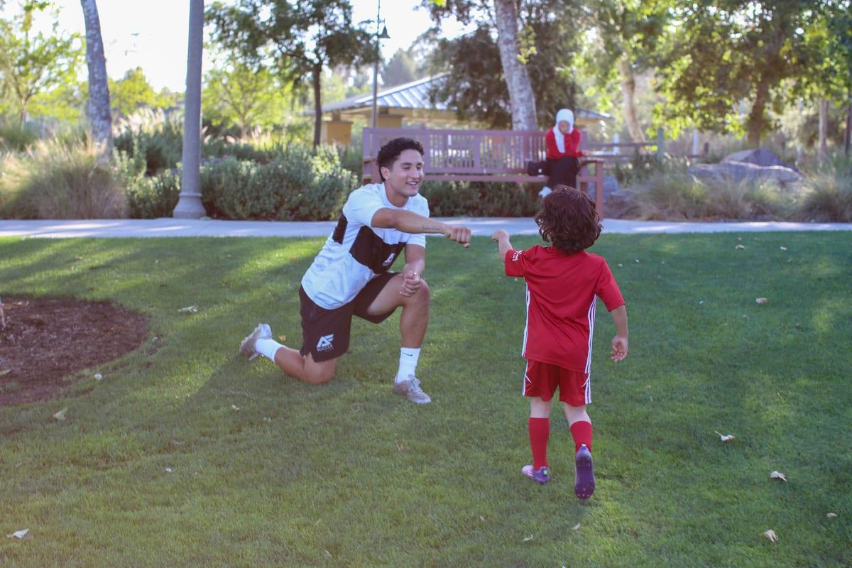 An AFC coach kneeling to fist-bump a young athlete during training